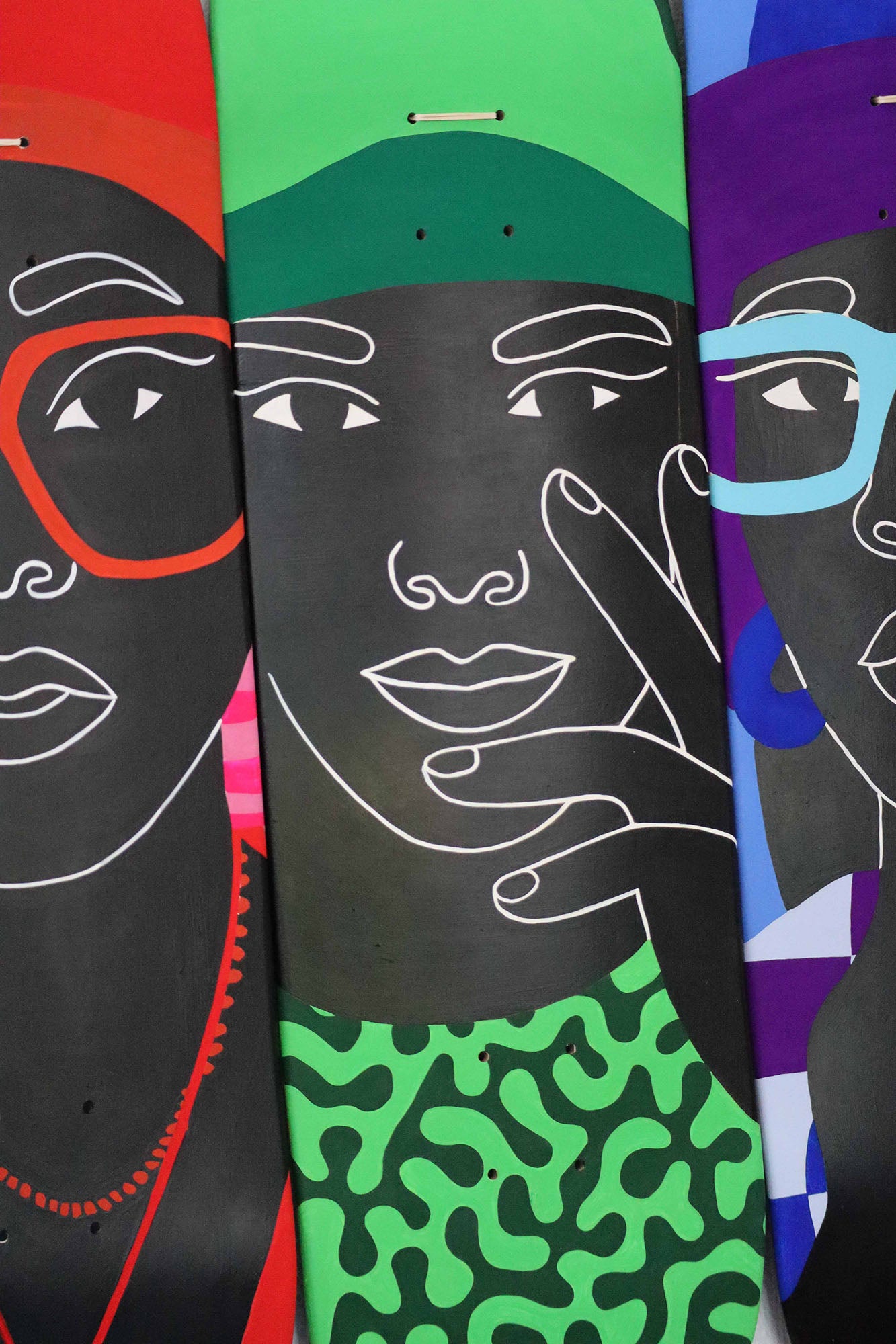 Three colorful skateboard decks with abstract face designs on a black background