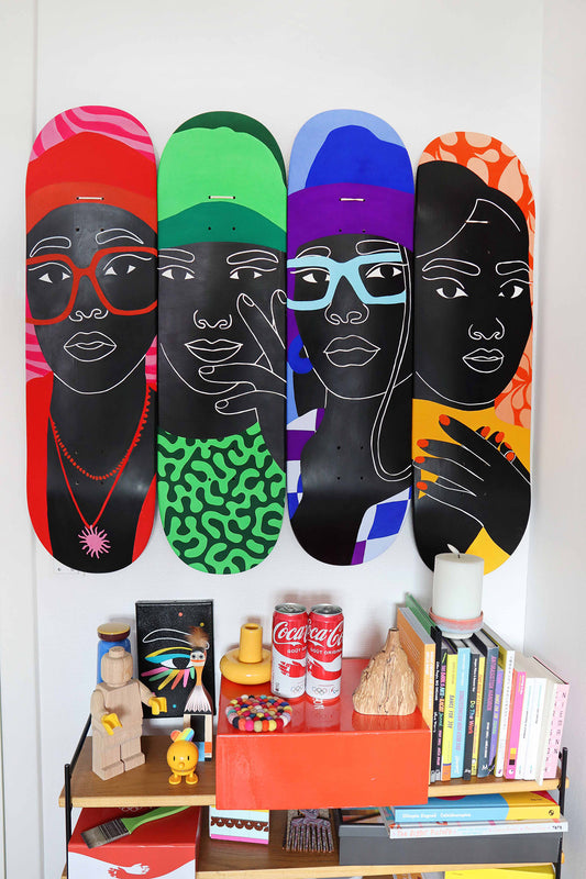 Colorful skateboard decks with artistic faces on a shelf with books and decor items from Aurélia Durand's atelier.